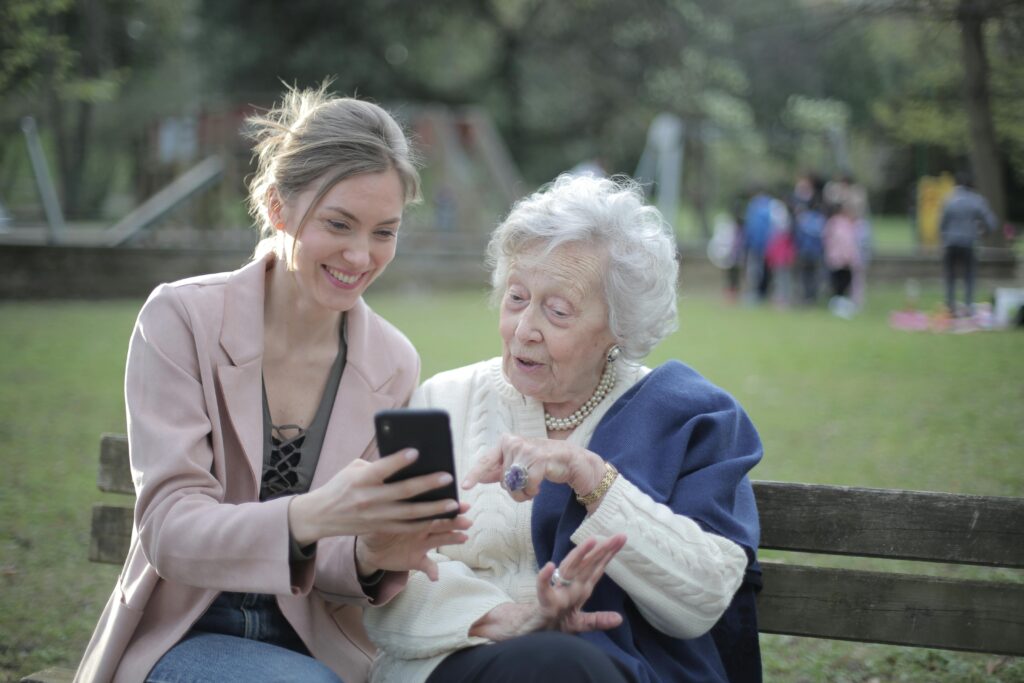 Cheerful senior mother and adult daughter using smartphone together outdoors