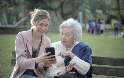 Cheerful senior mother and adult daughter using smartphone together outdoors